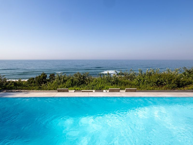An infinity edge swimming pool featuring timber decking and a direct, unobstructed view of the ocean.