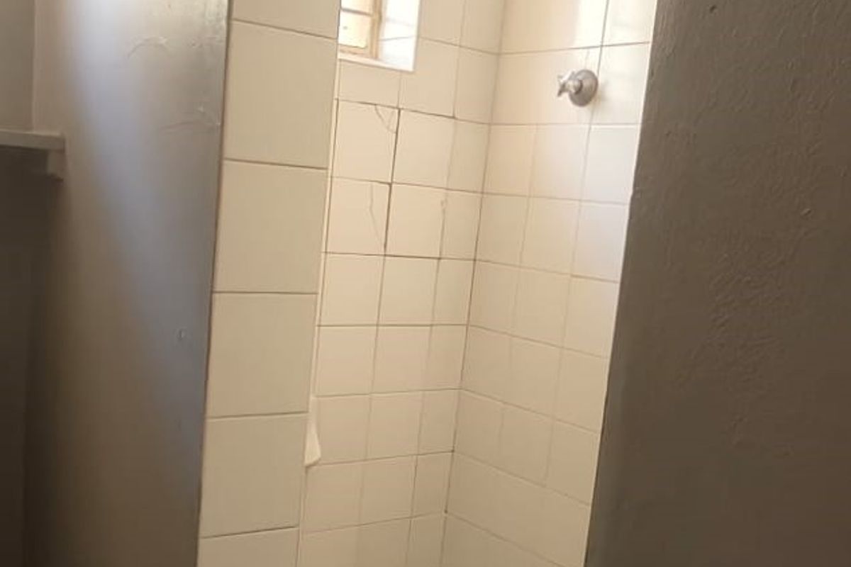A compact shower stall featuring white wall tiles, a mosaic-style floor, and a standard shower head fixture.