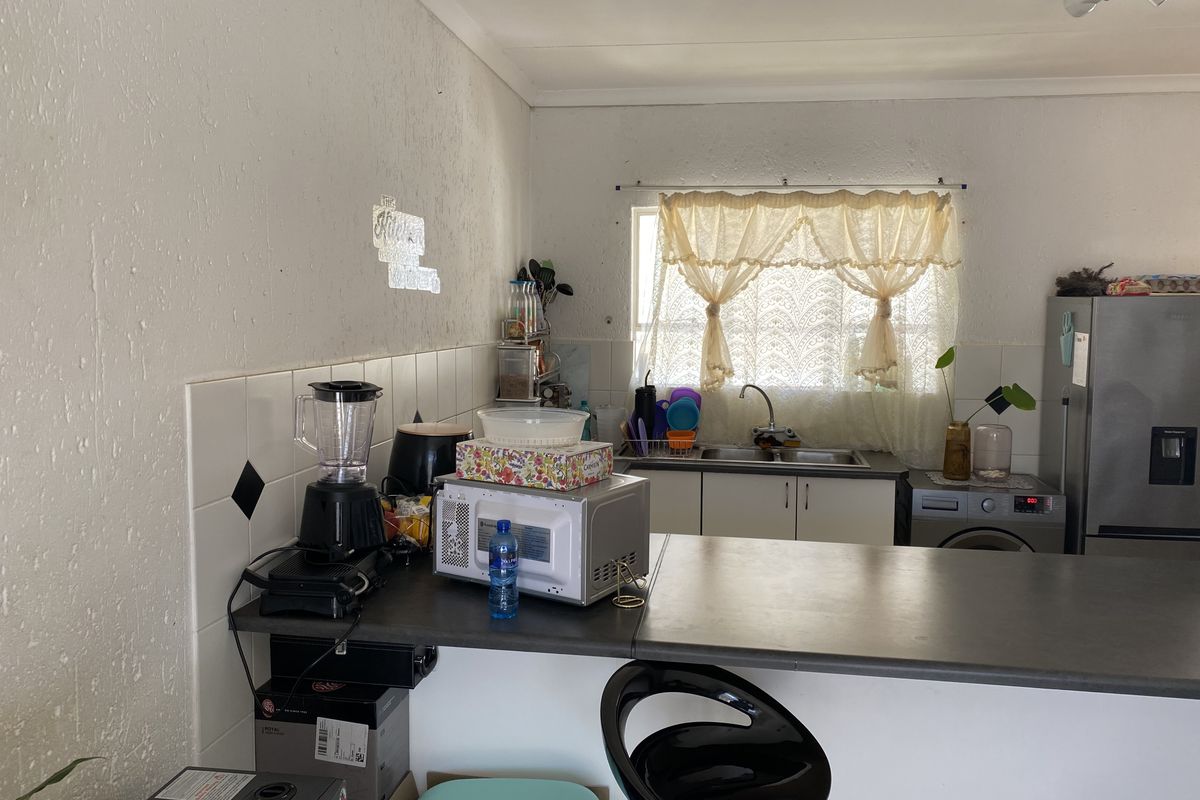 A compact kitchen featuring a breakfast bar, built-in cabinetry, a double sink, and tiled splashbacks, offering a functional layout for a flat.