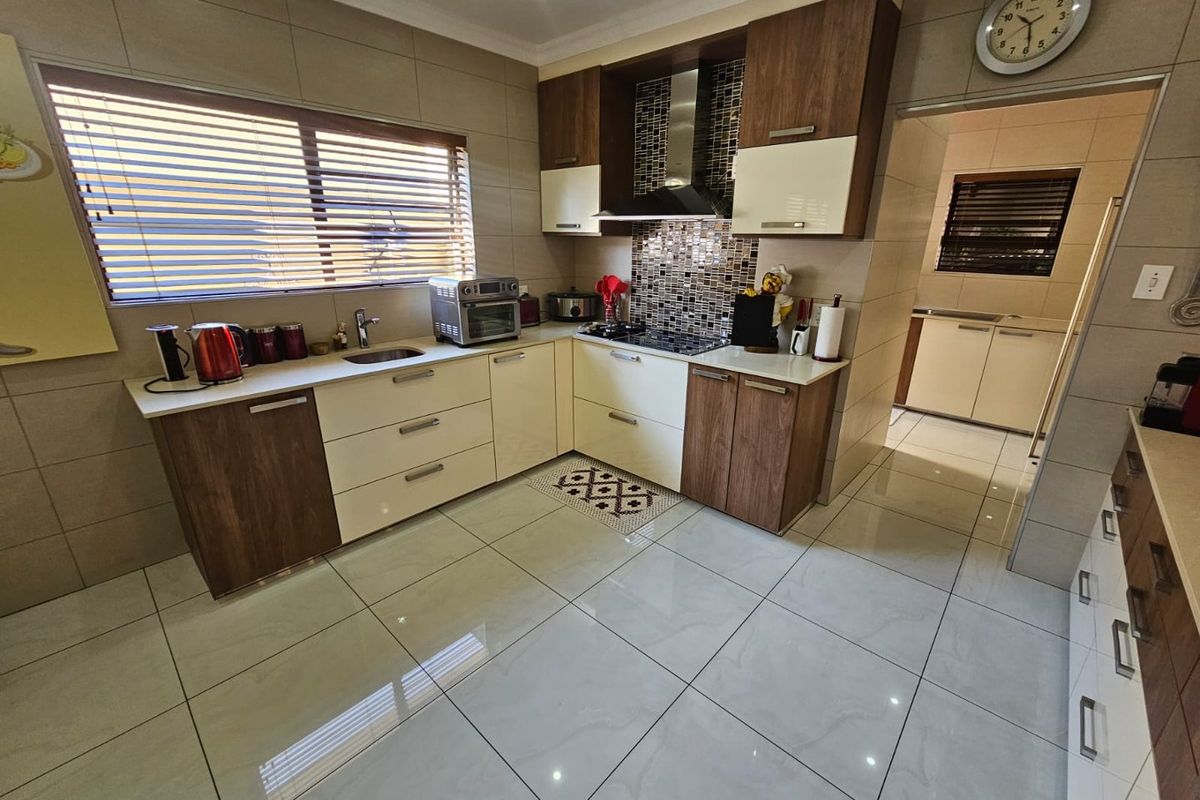 Modern kitchen featuring two-tone cabinetry, stone countertops, tiled splashback, built-in hob, and extractor fan, with an adjacent scullery area.