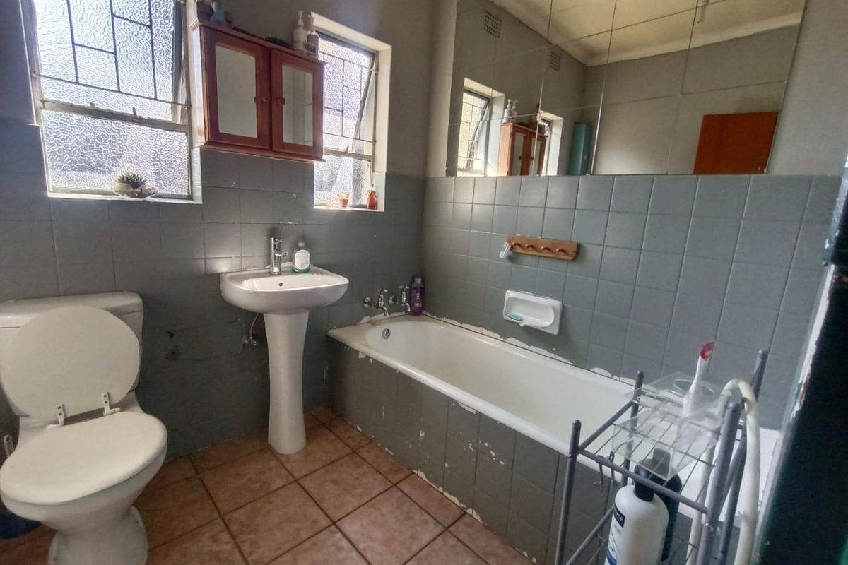 A dated bathroom featuring a pedestal basin, standard bathtub, and wall-mounted mirror, requiring cosmetic updates to modernize the space.