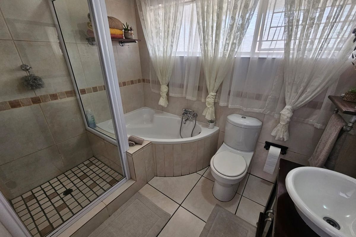 A functional bathroom featuring a corner bathtub, a separate glass-enclosed shower, a toilet, and a vanity basin with tiled walls and flooring.