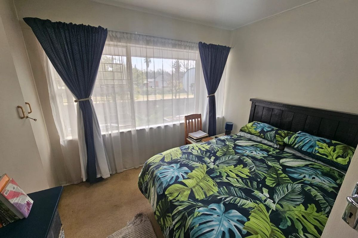A standard bedroom featuring a large window with curtain tracks and carpeted flooring.