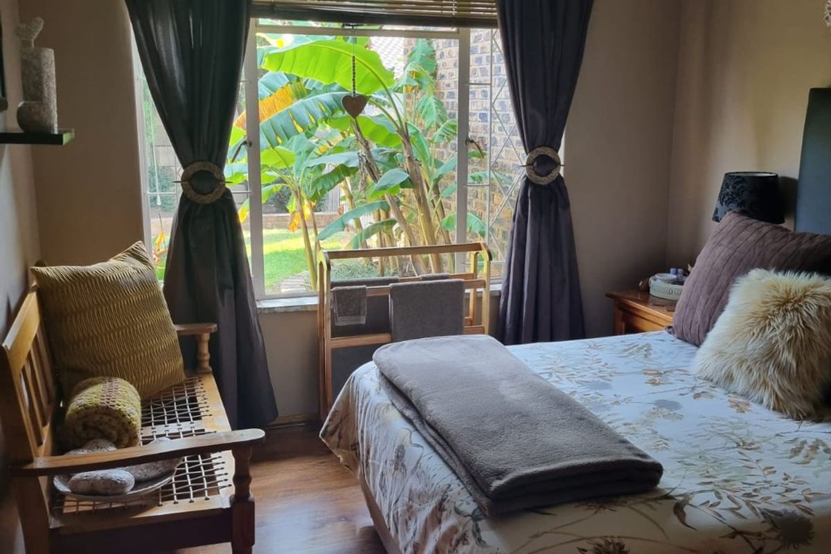 A cozy bedroom featuring laminate flooring, a ceiling fan, and a large window overlooking a garden area.