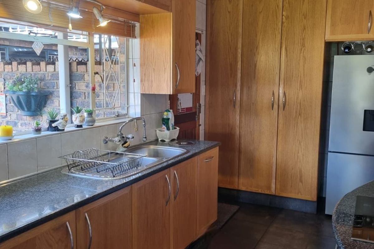 A functional kitchen featuring timber cabinetry, granite countertops, a double sink, and a distinctive timber-paneled ceiling with integrated track lighting.