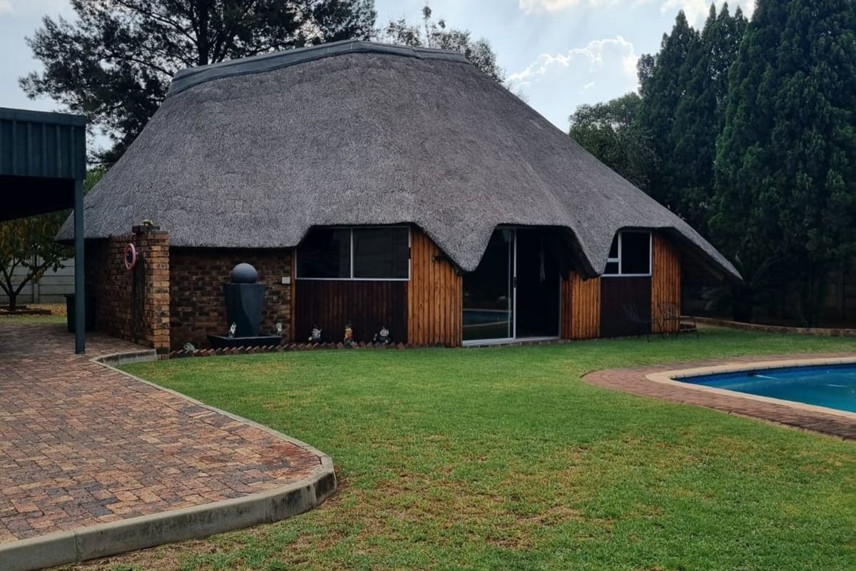 A well-maintained thatched-roof dwelling featuring brick and timber cladding, set within a landscaped garden with a swimming pool and paved patio area.