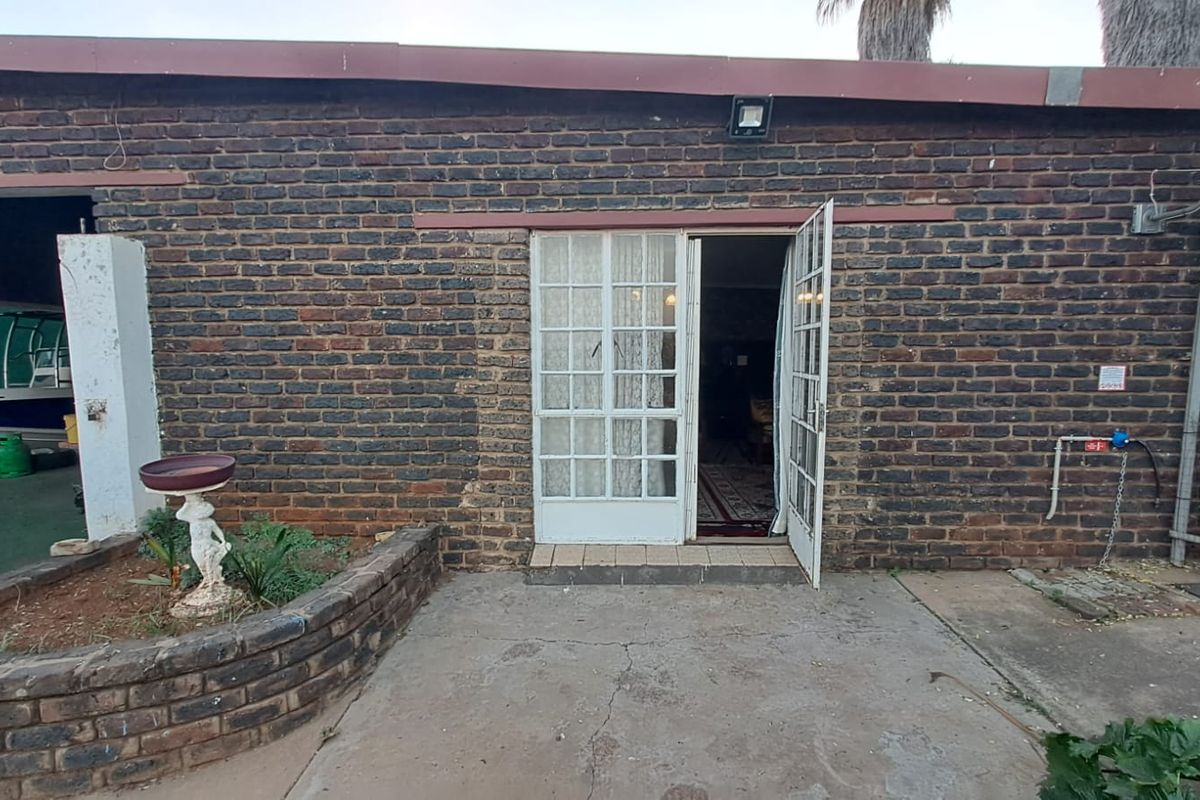 Rear exterior view of the property featuring a brick facade, concrete patio area, and double glass-paned doors leading into the interior.