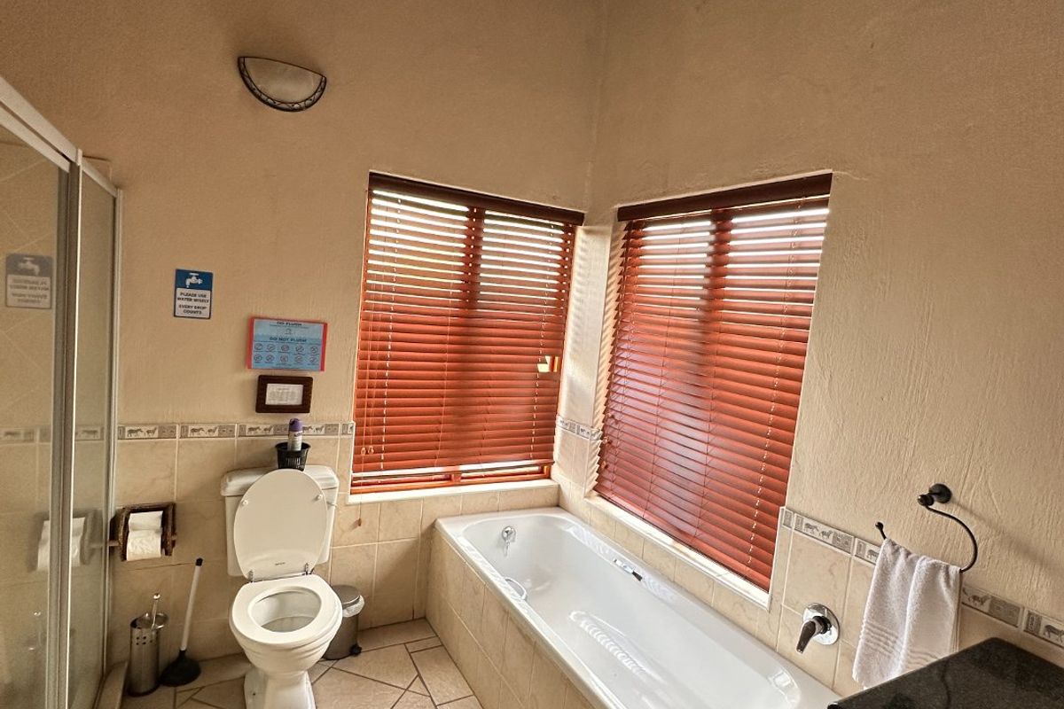 A well-appointed bathroom featuring a built-in bathtub, separate shower enclosure, toilet, and vanity, highlighted by a unique high-pitched thatched roof ceiling.