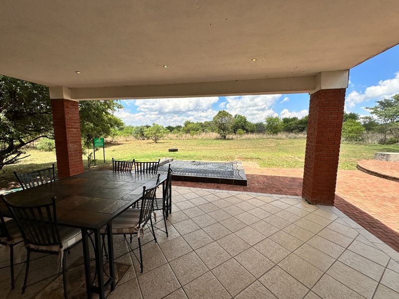 A covered outdoor patio featuring exposed brick columns, tiled flooring, and recessed lighting, overlooking a spacious garden area.