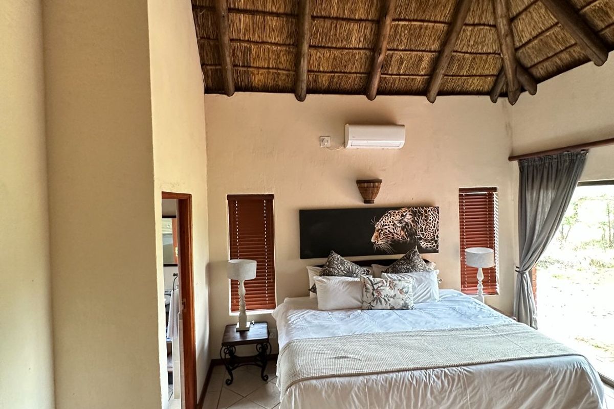 Spacious bedroom featuring a high vaulted thatched ceiling with exposed timber rafters, tiled flooring, and direct access to the outdoors via a sliding glass door.