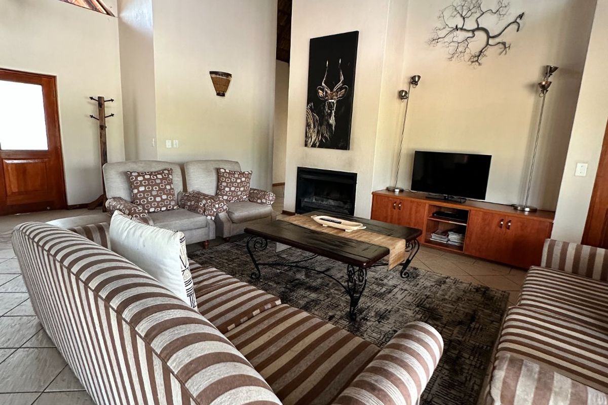 Spacious living room featuring a dramatic vaulted thatched ceiling, exposed timber beams, tiled flooring, and a cozy built-in fireplace.