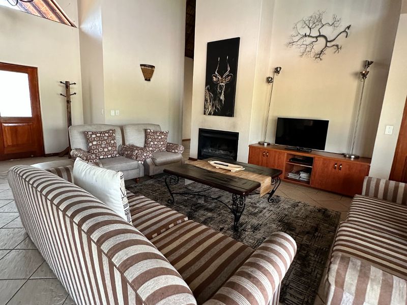 Spacious living room featuring a dramatic vaulted thatched ceiling, exposed timber beams, tiled flooring, and a cozy built-in fireplace.