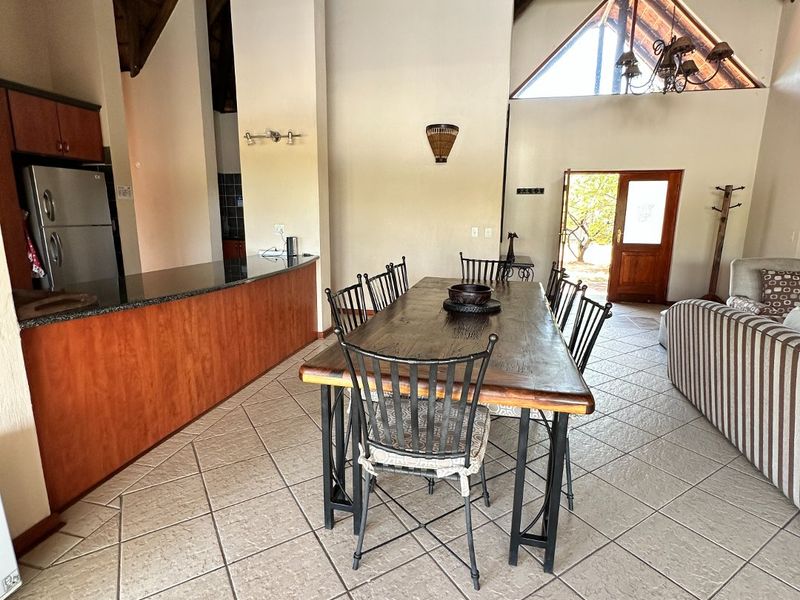 Spacious open-plan living and dining area featuring a high vaulted thatched ceiling, exposed timber beams, tiled flooring, and a granite-topped kitchen counter.