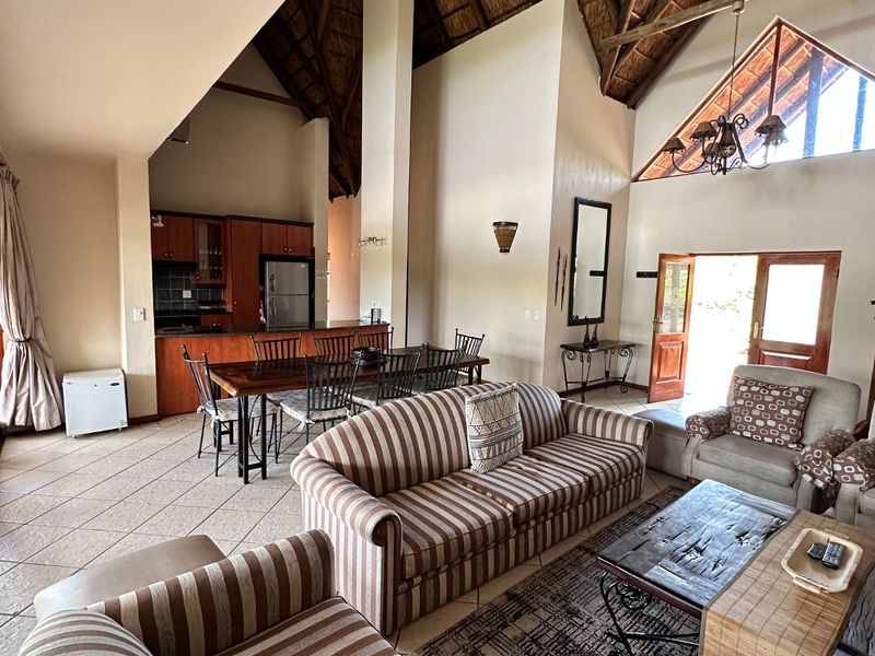 Spacious open-plan living and dining area featuring a high vaulted thatched ceiling with exposed timber trusses and direct access to the outdoors.