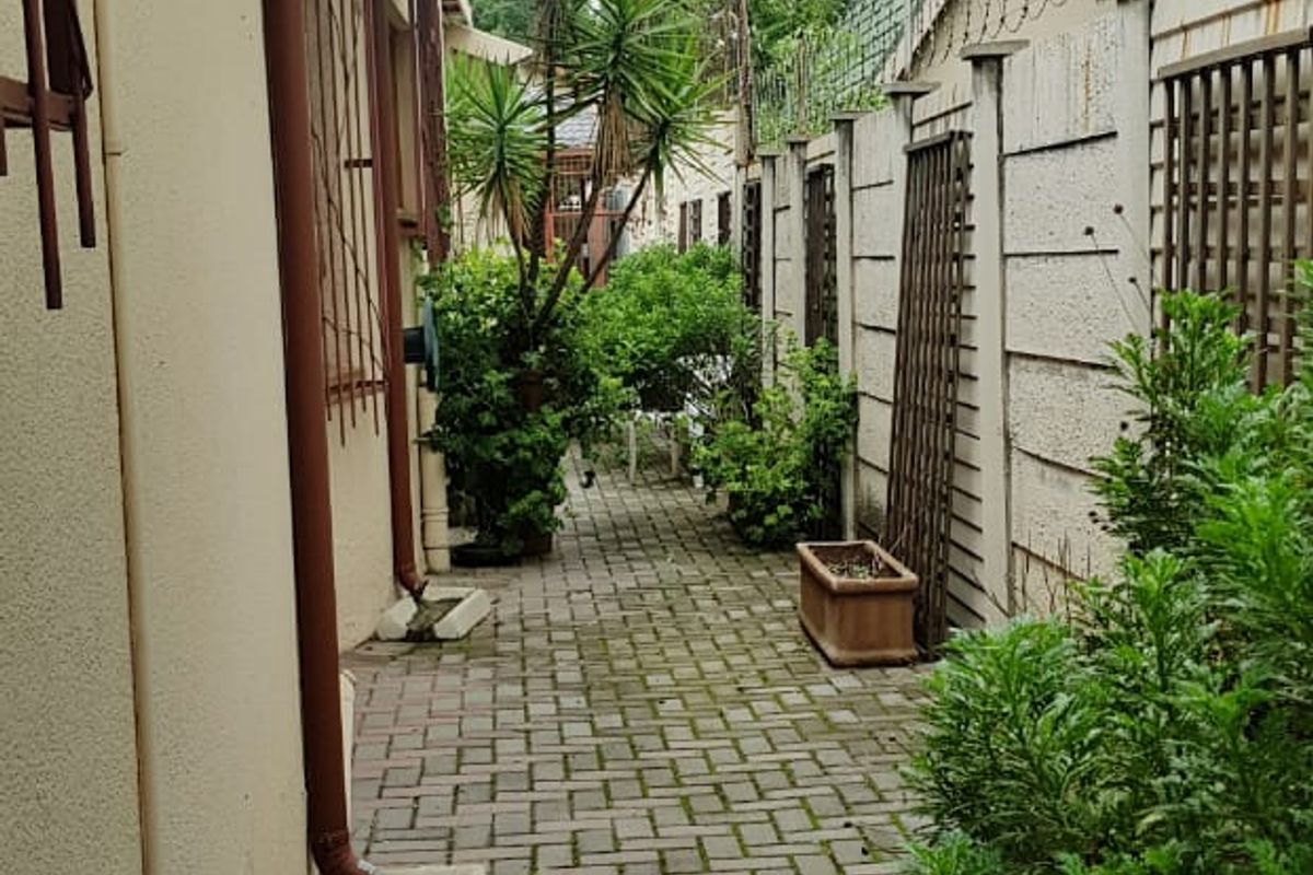 A narrow rear exterior walkway featuring paved flooring, perimeter boundary walls with security fencing, and functional drainage downpipes.