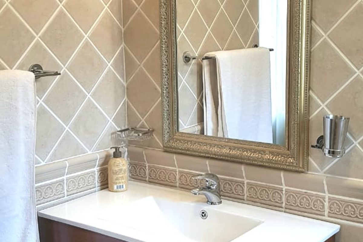 A well-maintained bathroom vanity area featuring a modern wooden cabinet, integrated basin, decorative wall tiling, and elegant wall-mounted lighting.