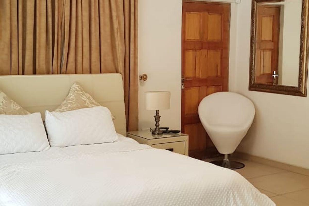 A well-lit bedroom featuring tiled flooring, a wooden door, and neutral wall finishes, providing a comfortable and functional living space.