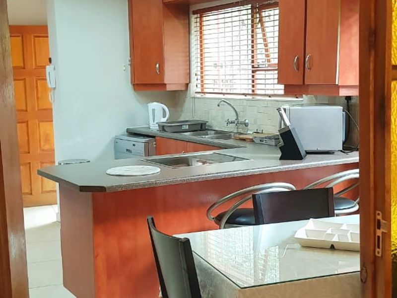 Open-plan kitchen and dining area featuring warm-toned cabinetry, tiled flooring, and functional counter space, viewed through a wooden door frame.