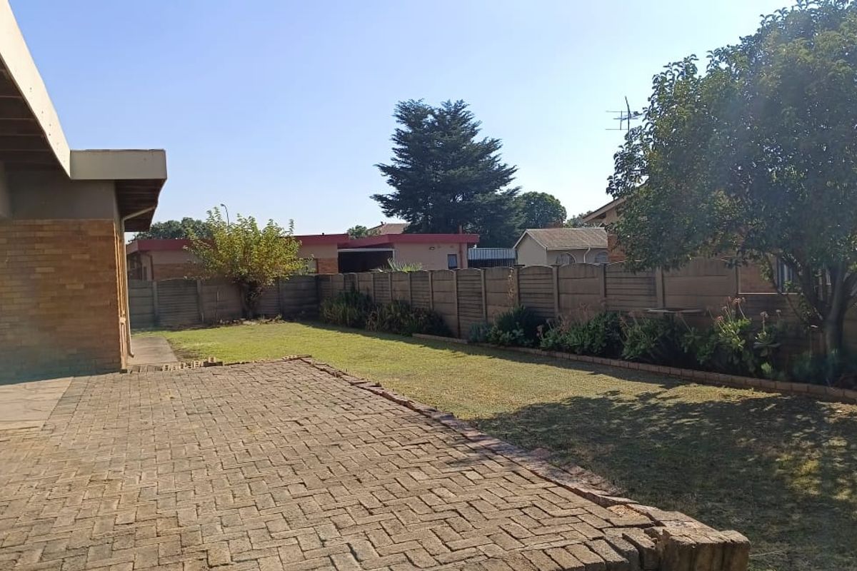 A spacious rear garden featuring a paved patio area, established lawn, and perimeter boundary walling.