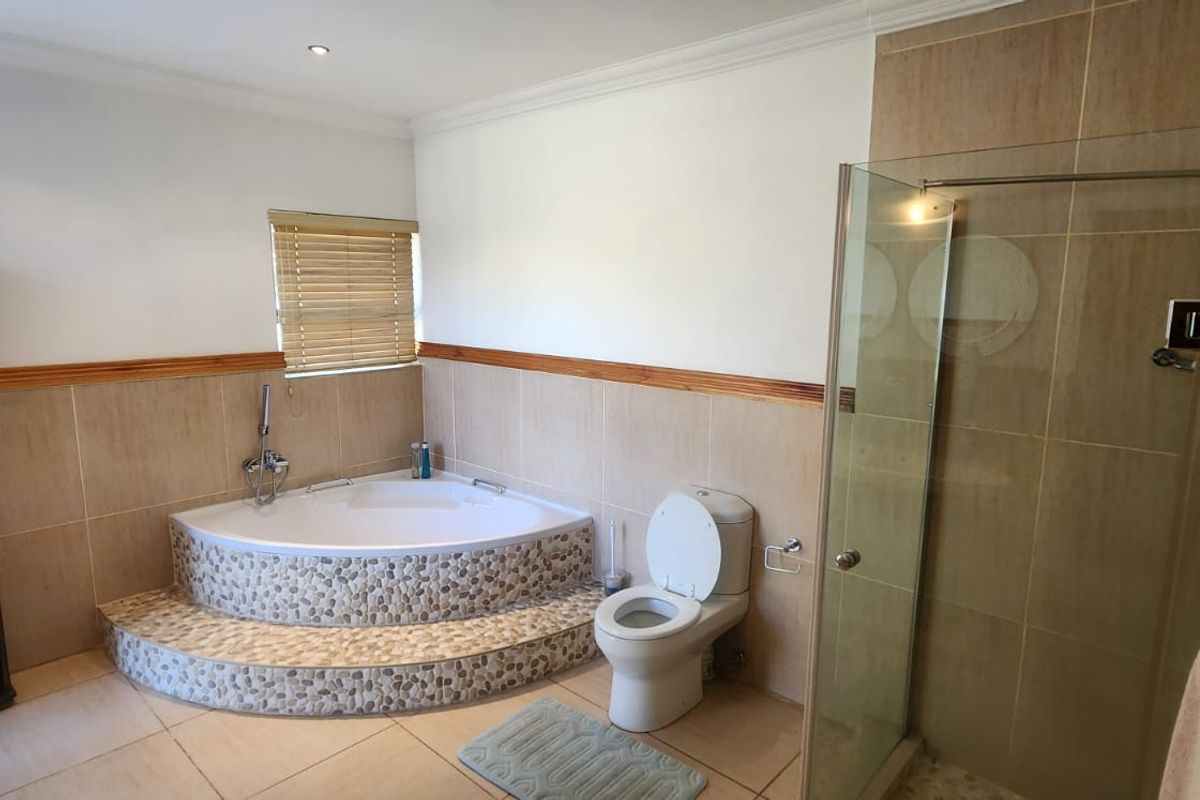 A bathroom featuring a corner soaking tub with pebble-tiled surround, a separate glass-enclosed shower, and a standard toilet.