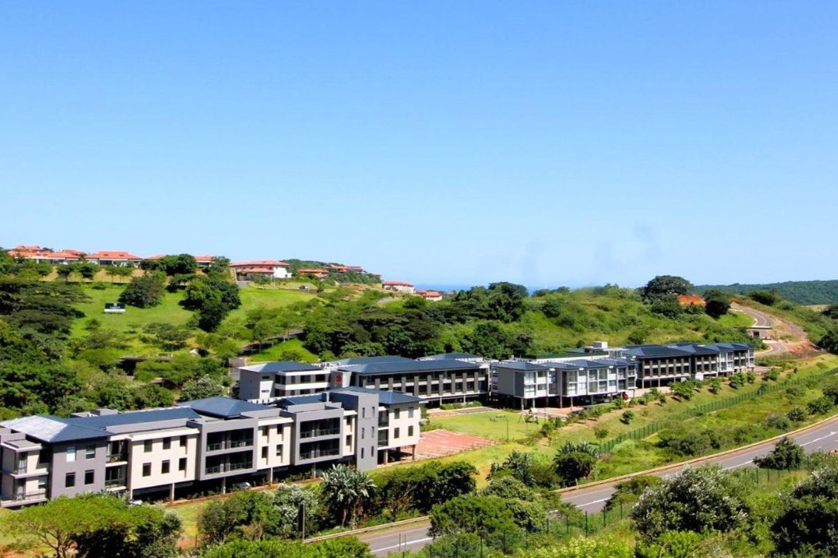 Aerial view of a modern residential apartment complex situated in a landscaped estate with surrounding road access and greenery.