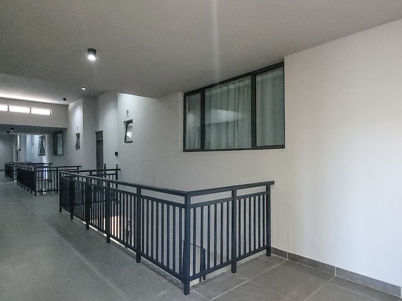 A modern, well-maintained apartment building hallway featuring tiled flooring, metal balustrades, and recessed ceiling lighting.