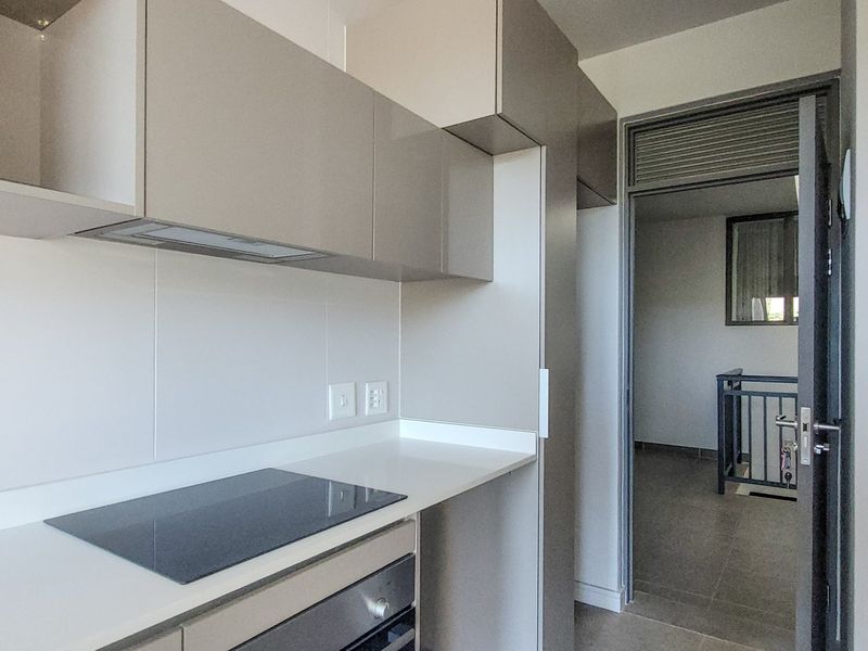 Modern kitchen featuring sleek built-in cabinetry, stone countertops, an integrated electric hob, and an oven, offering a clean and functional cooking space.