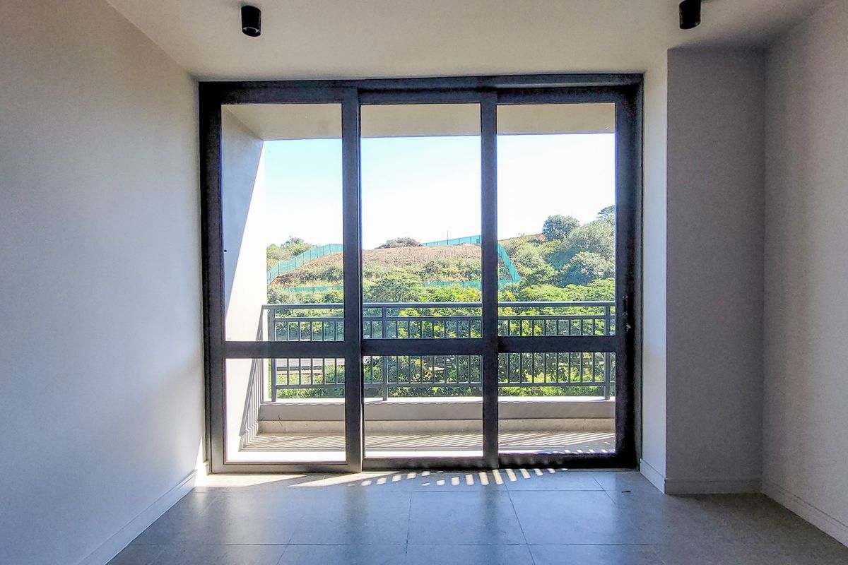 A bright, empty living area featuring large sliding glass doors that open onto a balcony with scenic green views.