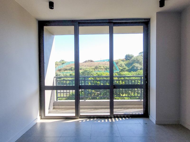 A bright, empty living area featuring large sliding glass doors that open onto a balcony with scenic green views.