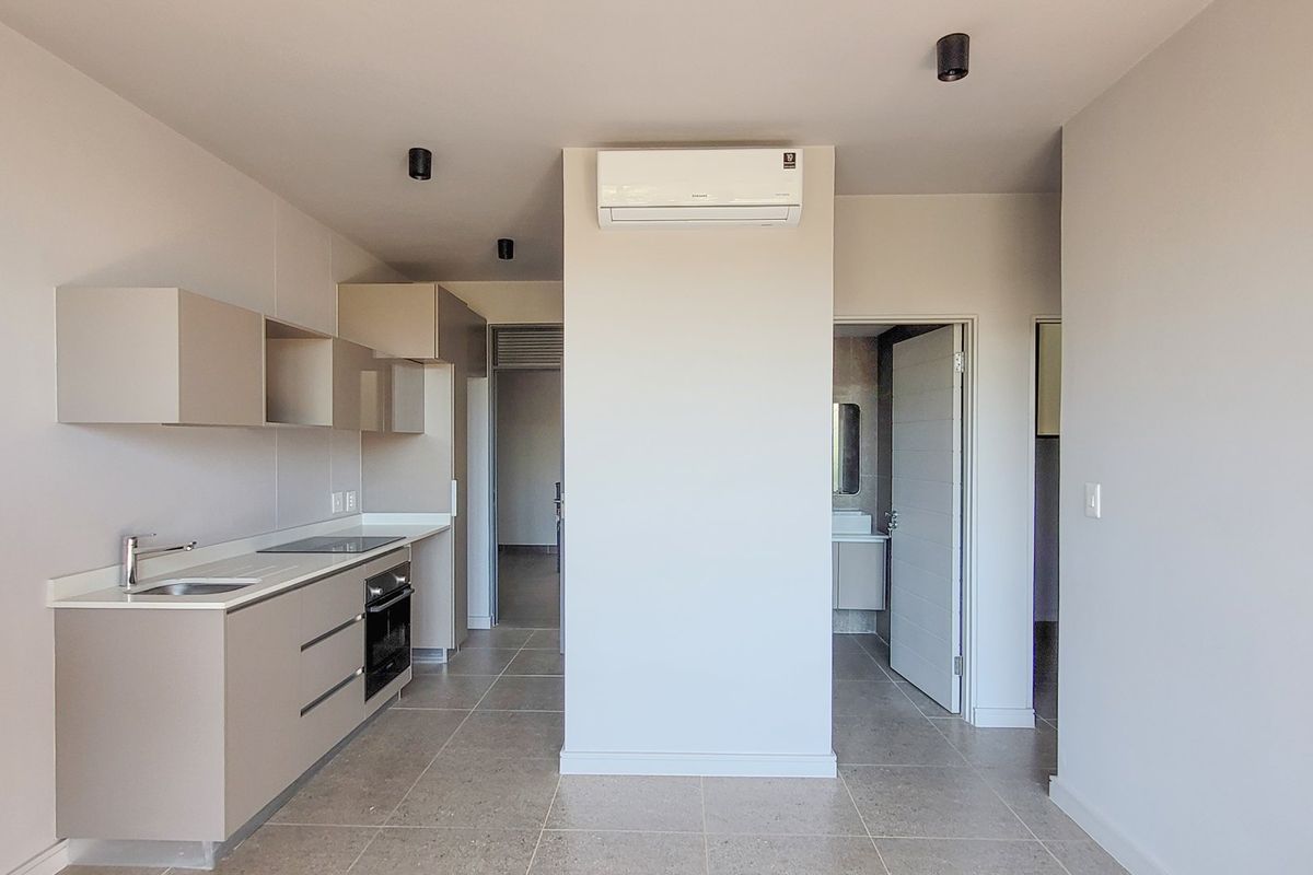 Modern kitchen featuring sleek built-in cabinetry, integrated oven, electric hob, and a split-system air conditioner, finished with neutral tiled flooring.