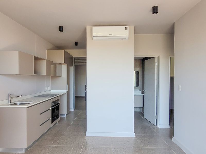 Modern kitchen featuring sleek built-in cabinetry, integrated oven, electric hob, and a split-system air conditioner, finished with neutral tiled flooring.