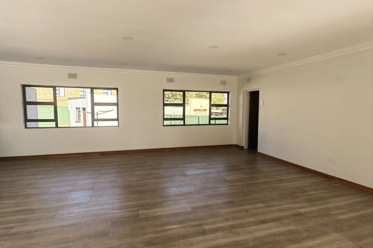 Spacious, light-filled living area featuring modern wood-look tile flooring, recessed ceiling lighting, and large windows providing ample natural light.