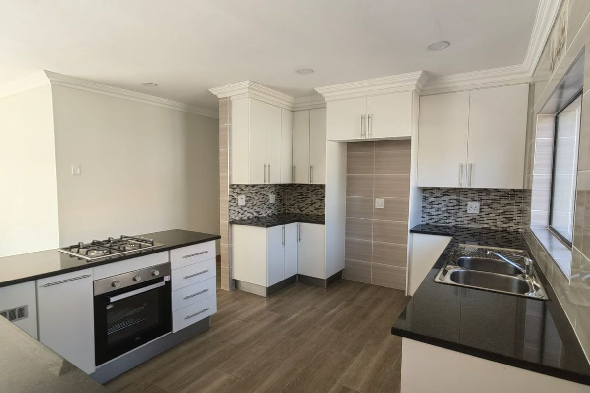 Modern kitchen featuring white cabinetry, dark granite countertops, built-in gas hob, oven, and double stainless steel sink with tiled backsplash.