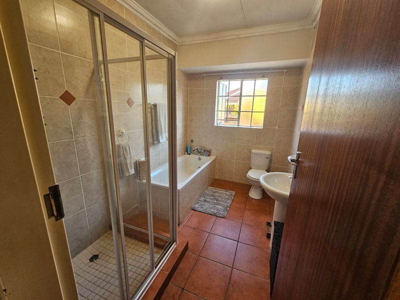 A functional bathroom featuring a separate shower enclosure, a built-in bathtub, a pedestal basin, and a toilet with tiled flooring and walls.