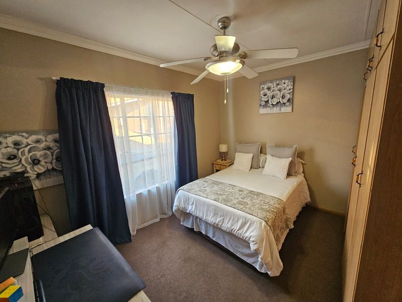 A cozy bedroom featuring built-in wooden cabinetry, a ceiling fan, and carpeted flooring, providing a functional and comfortable living space.