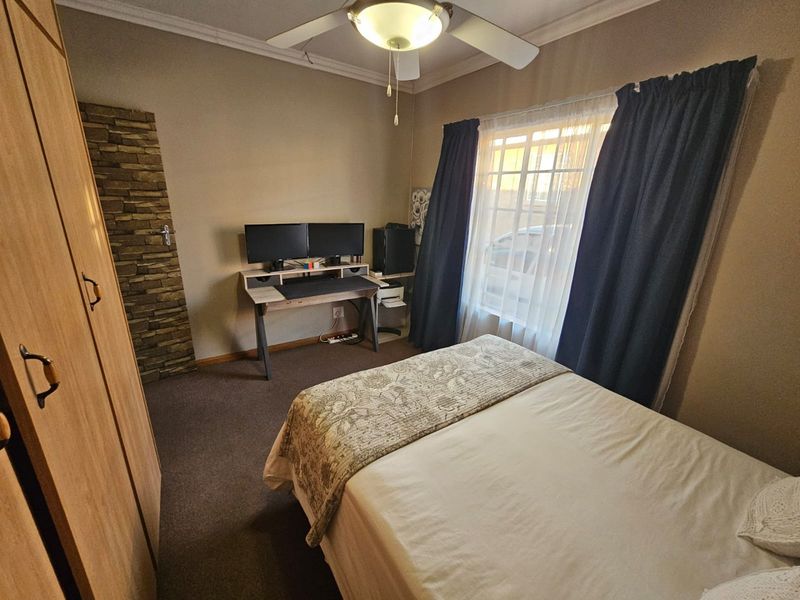 A functional bedroom featuring a built-in wardrobe, ceiling fan, and carpeted flooring, providing a comfortable and practical living space.