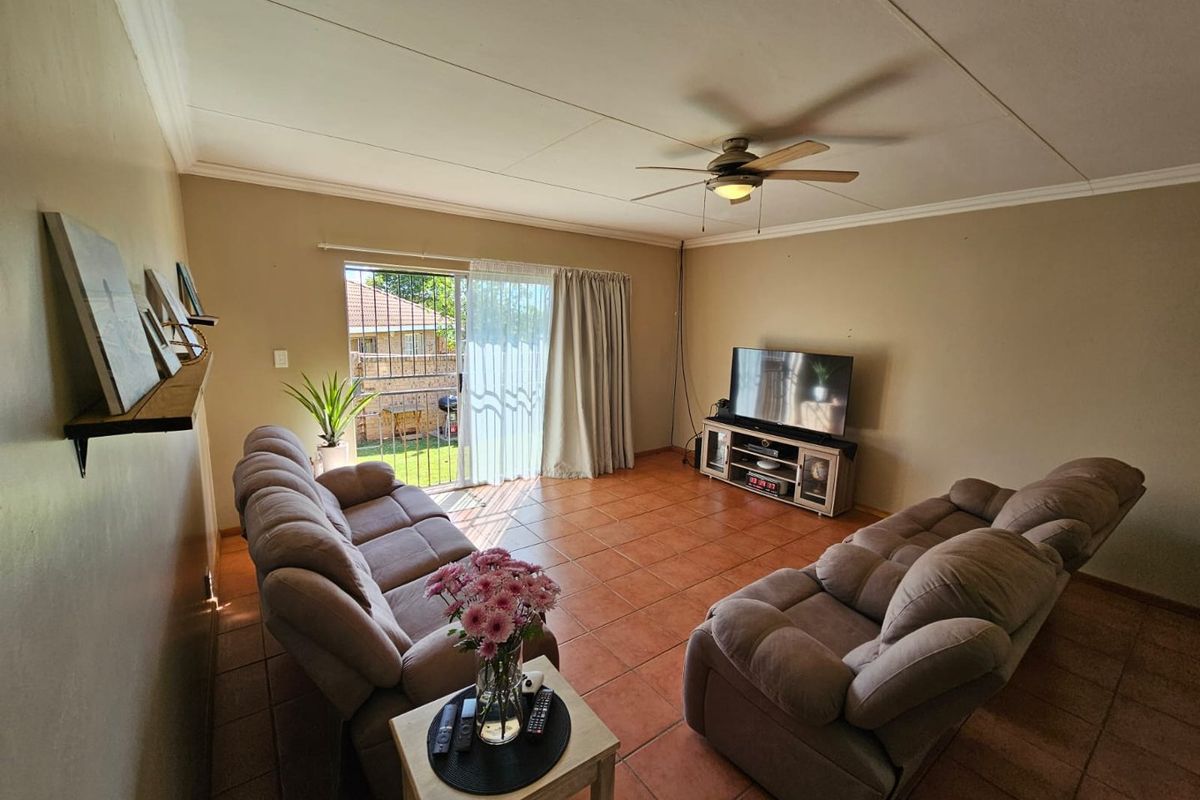 A living room featuring terracotta floor tiles, a ceiling fan, and sliding glass doors providing access to the outdoor area.