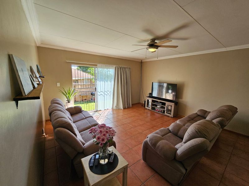 A living room featuring terracotta floor tiles, a ceiling fan, and sliding glass doors providing access to the outdoor area.