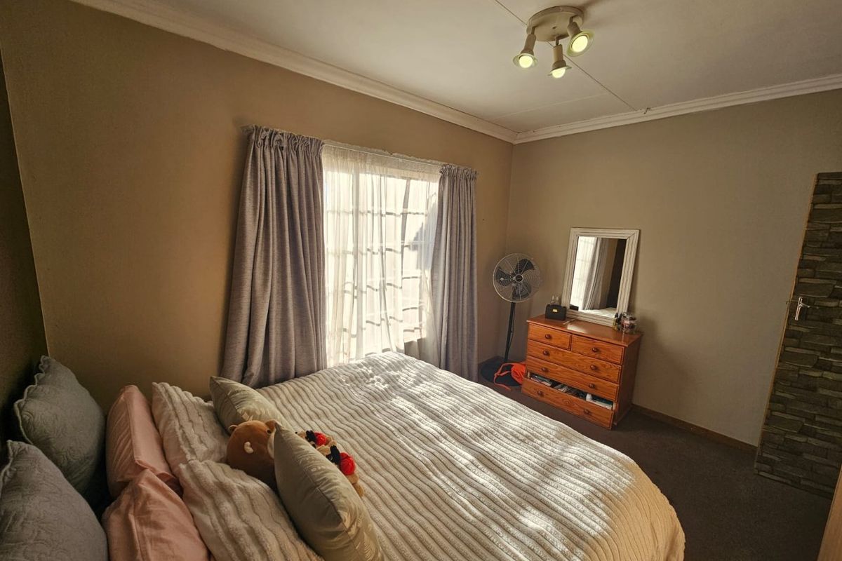 A bedroom featuring neutral wall tones, carpeted flooring, and a window with curtain treatments, providing a comfortable and functional living space.
