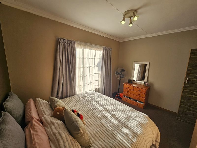 A bedroom featuring neutral wall tones, carpeted flooring, and a window with curtain treatments, providing a comfortable and functional living space.