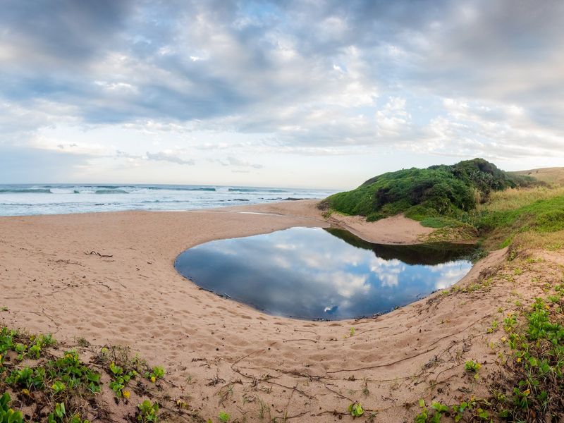 A scenic panoramic view of the coastal landscape, featuring sandy terrain, a natural water feature, and direct access to the ocean.