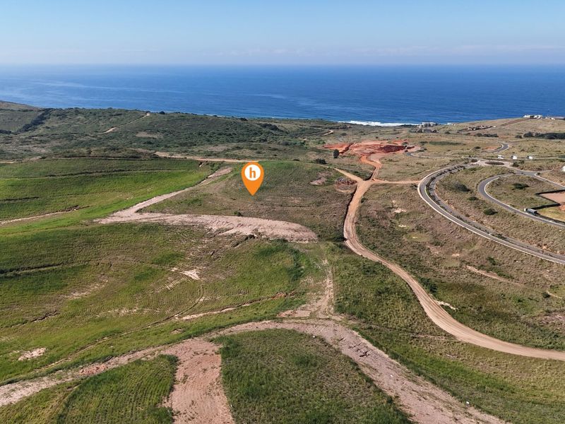 Aerial view of a vacant residential plot featuring rolling green landscape and coastal ocean views in a developing estate.