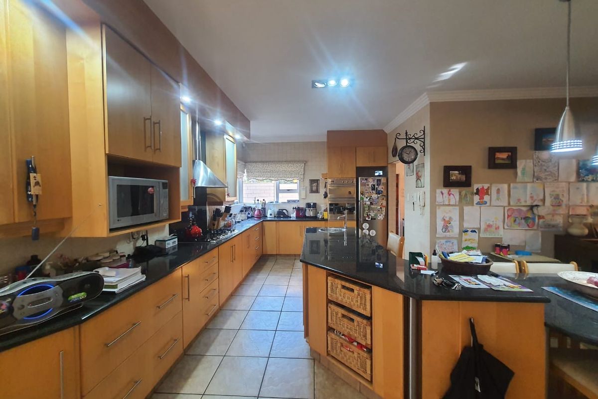 Spacious kitchen featuring light wood cabinetry, dark granite countertops, a central island with breakfast bar, and integrated stainless steel appliances.