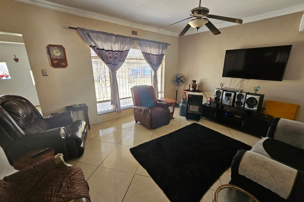 A spacious living room featuring large format floor tiles, a ceiling fan, and a wall-mounted television setup.