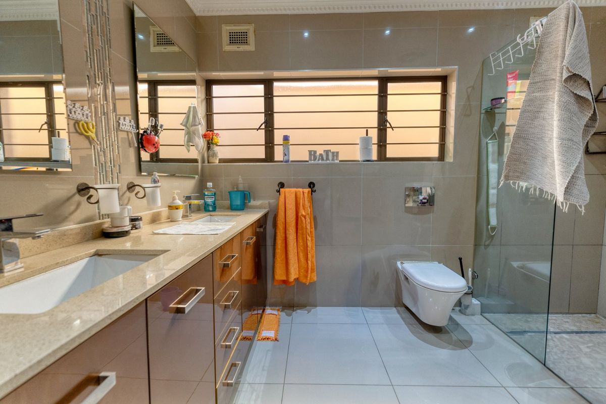 Modern bathroom featuring a double vanity with stone countertop, wall-mounted toilet, and a glass-enclosed walk-in shower with neutral floor-to-ceiling tiling.