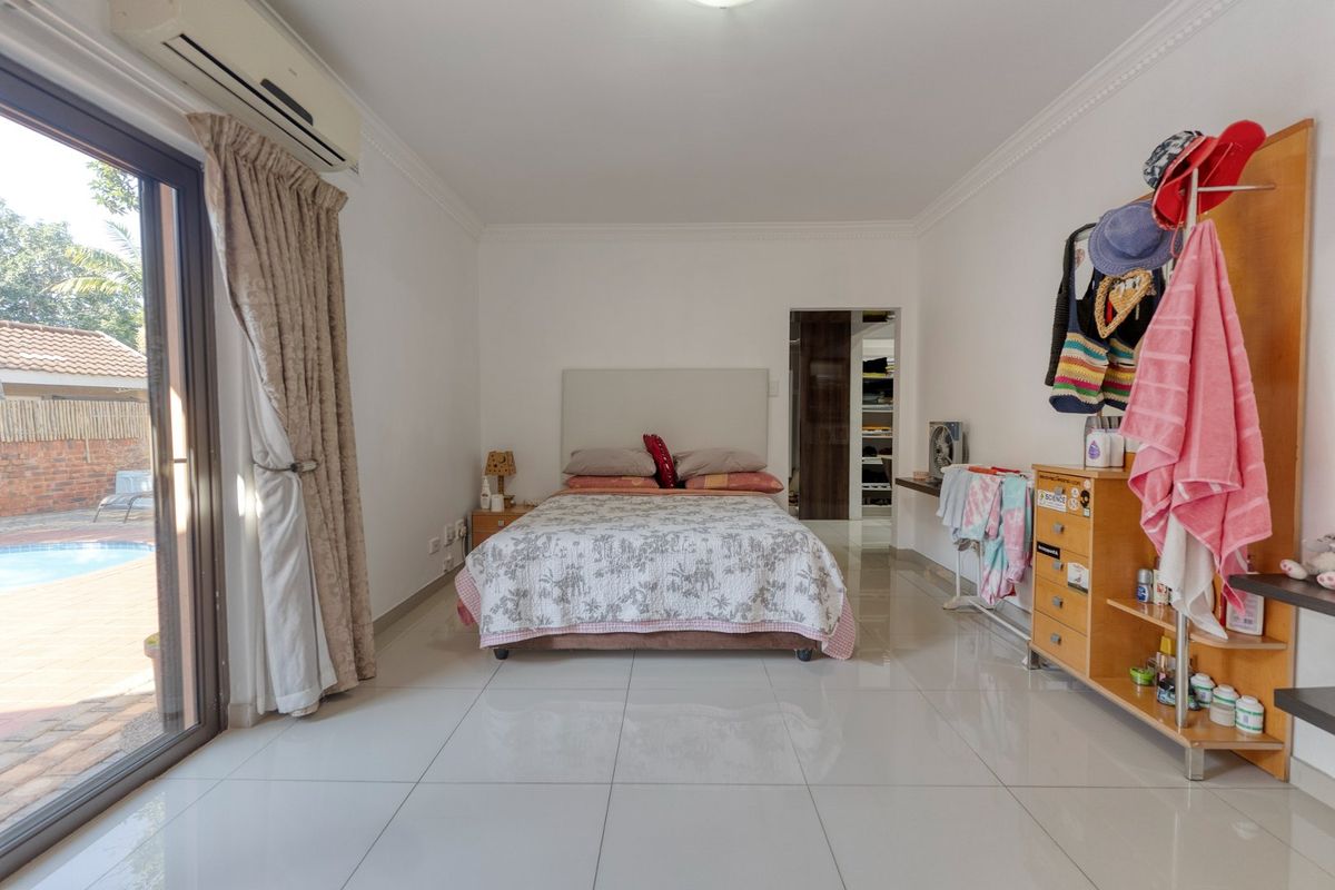 Spacious bedroom featuring large sliding glass doors with direct access to the pool area, tiled flooring, and an integrated air conditioning unit.