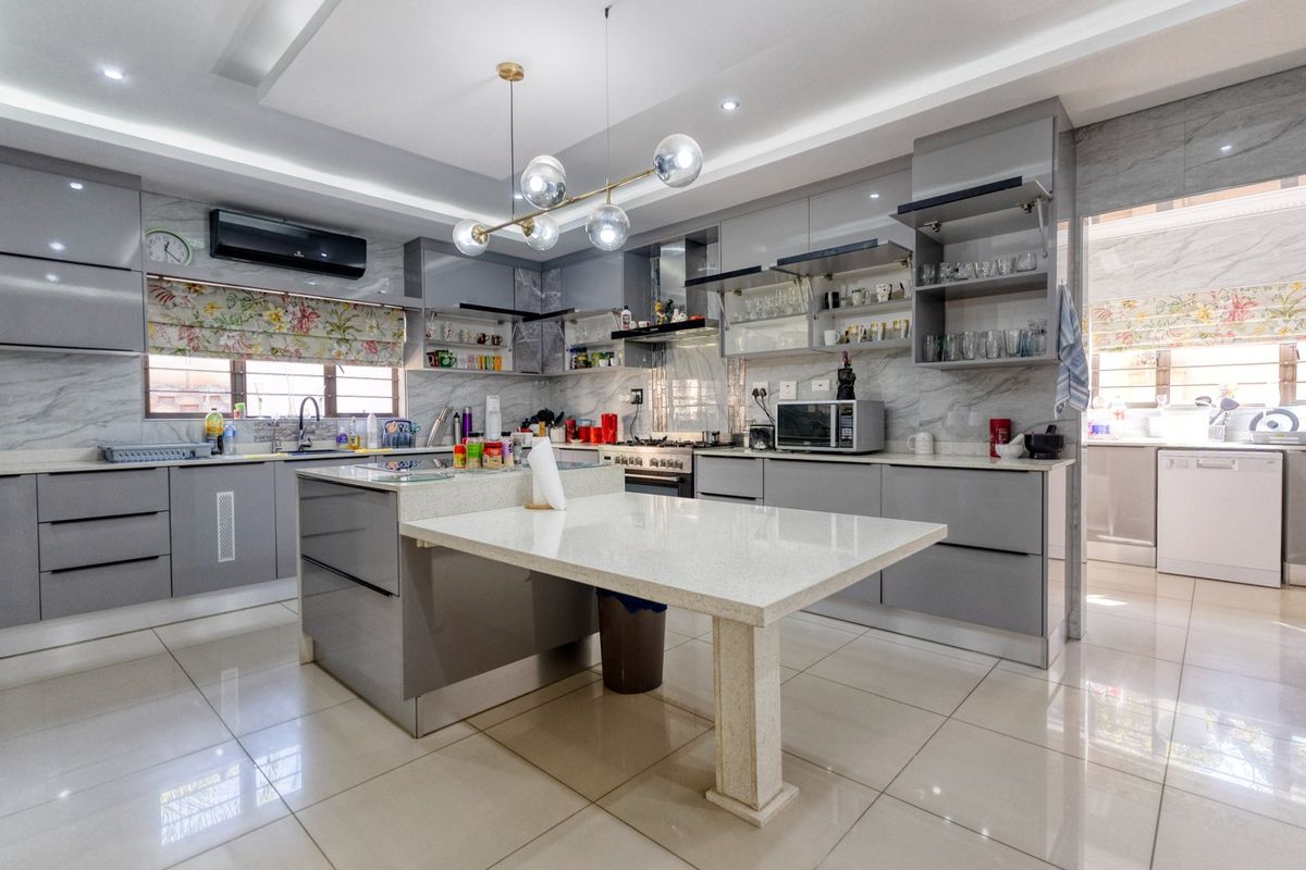 Modern kitchen featuring high-gloss grey cabinetry, stone countertops, a central island with integrated dining table, and tiled flooring.