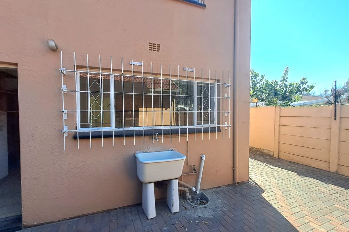 Rear exterior area of the townhouse featuring a paved courtyard, a utility sink, and security bars on the window.