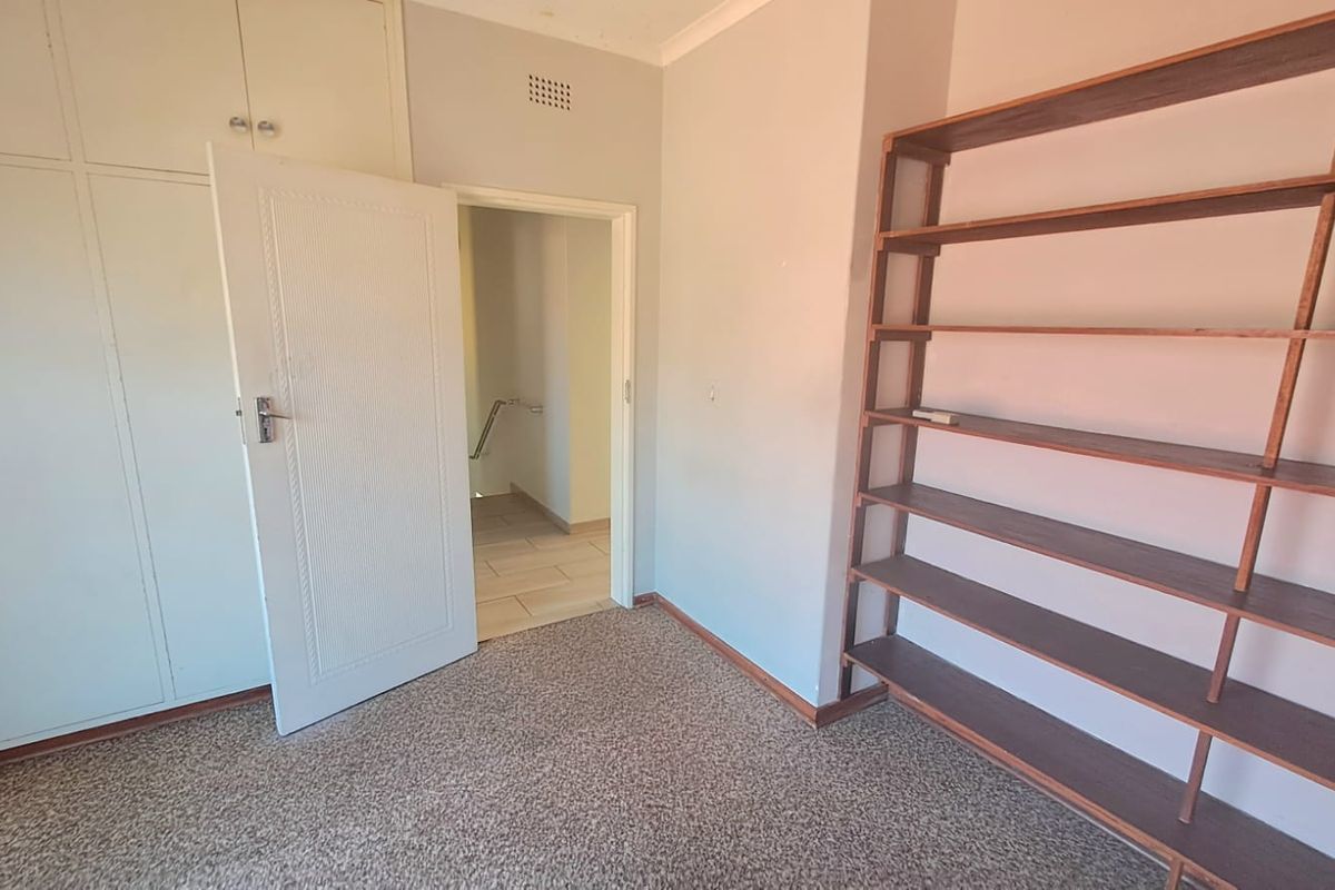 A bedroom featuring built-in cupboards and carpeted flooring, with an open doorway leading to a hallway.