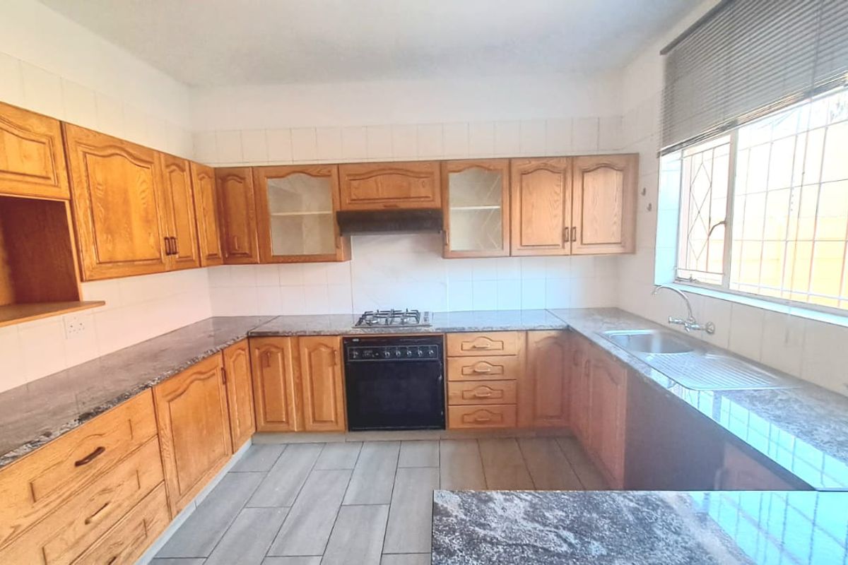 A functional kitchen featuring traditional timber cabinetry, granite-look countertops, a built-in oven with gas hob, and a stainless steel sink.